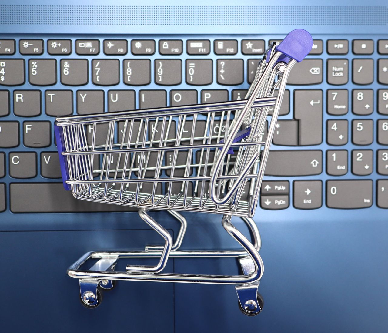 about-us A miniature shopping cart placed on a laptop keyboard symbolizing online shopping and e-commerce.
